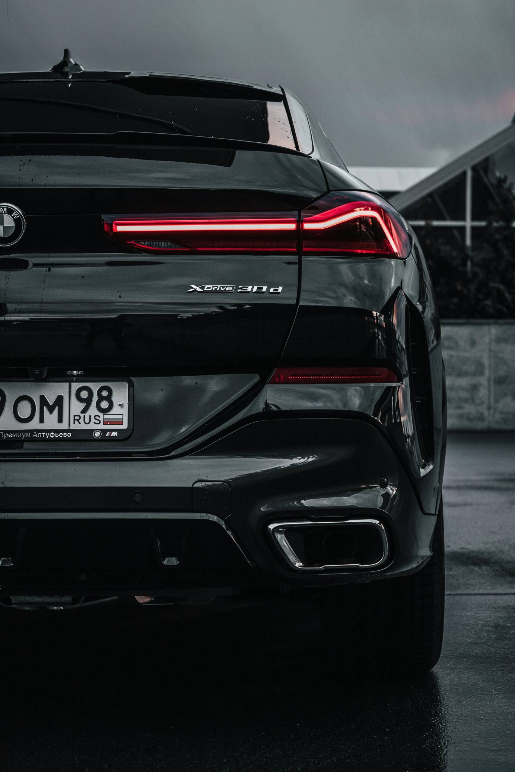 A dark, close-up view of a parked BMW showcasing its illuminated tail lights and shiny emblem.